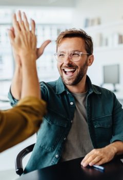 Successful business people giving each other a high five in a meeting. Two young business professionals celebrating teamwork in an office.